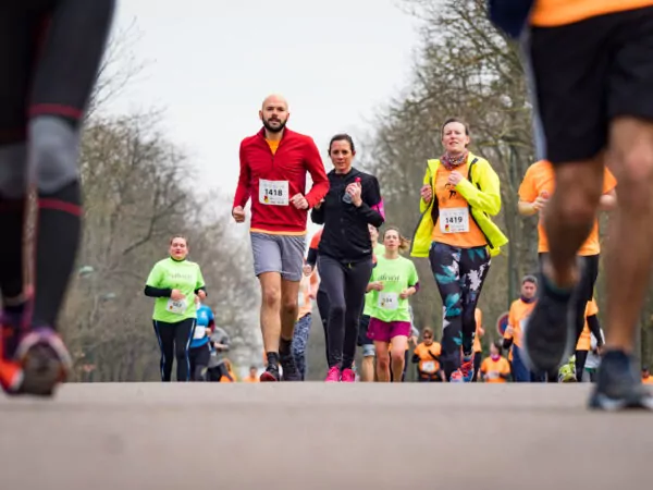 Des coureurs portant des dossards participent à une course sur route en plein air. L'accent est mis sur trois coureurs au premier plan, tandis que d'autres participants et des arbres dénudés sont visibles à l'arrière-plan. Le temps est frais et couvert. - Rotary Club Paris Agora