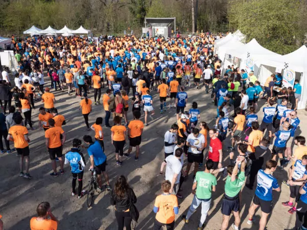Une grande foule de personnes vêtues de chemises de sport colorées se rassemblent en plein air près de tentes blanches, se préparant à une course ou à un événement ; certains s'étirent, marchent ou discutent sous un ciel ensoleillé. - Rotary Club Paris Agora