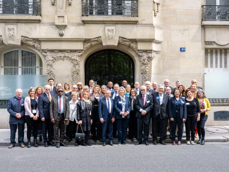 A group of approximately 35 people dressed in casual or business attire, including members of the Intercountry Committees, pose together for a photo outside a historic stone building with ornamental details and arched windows. - Rotary Club Paris Agora