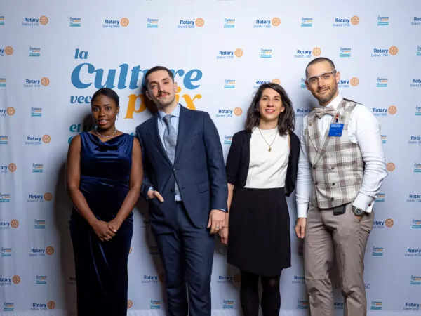 Four adults stand side-by-side, dressed in formal wear, posing in front of a backdrop adorned with Rotary International logos and French text - an image that captures a historic meeting for the future of multilateralism. - Rotary Club Paris Agora