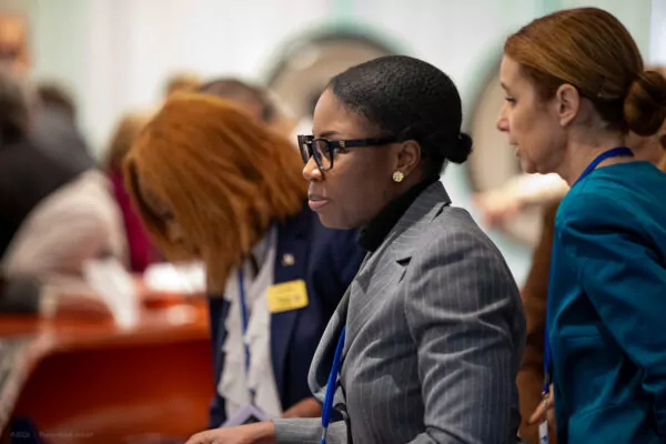 A woman in a gray pinstripe suit and glasses is focused, standing next to other people at a professional event centered on multilateralism. The people around her are engaged in conversation or looking at documents. - Rotary Club Paris Agora