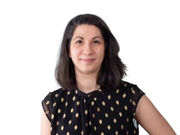 A woman with medium-length brown hair smiles slightly at the camera. She is wearing a sleeveless black top with a gold oval pattern. The background is white. - Rotary Club Paris Agora