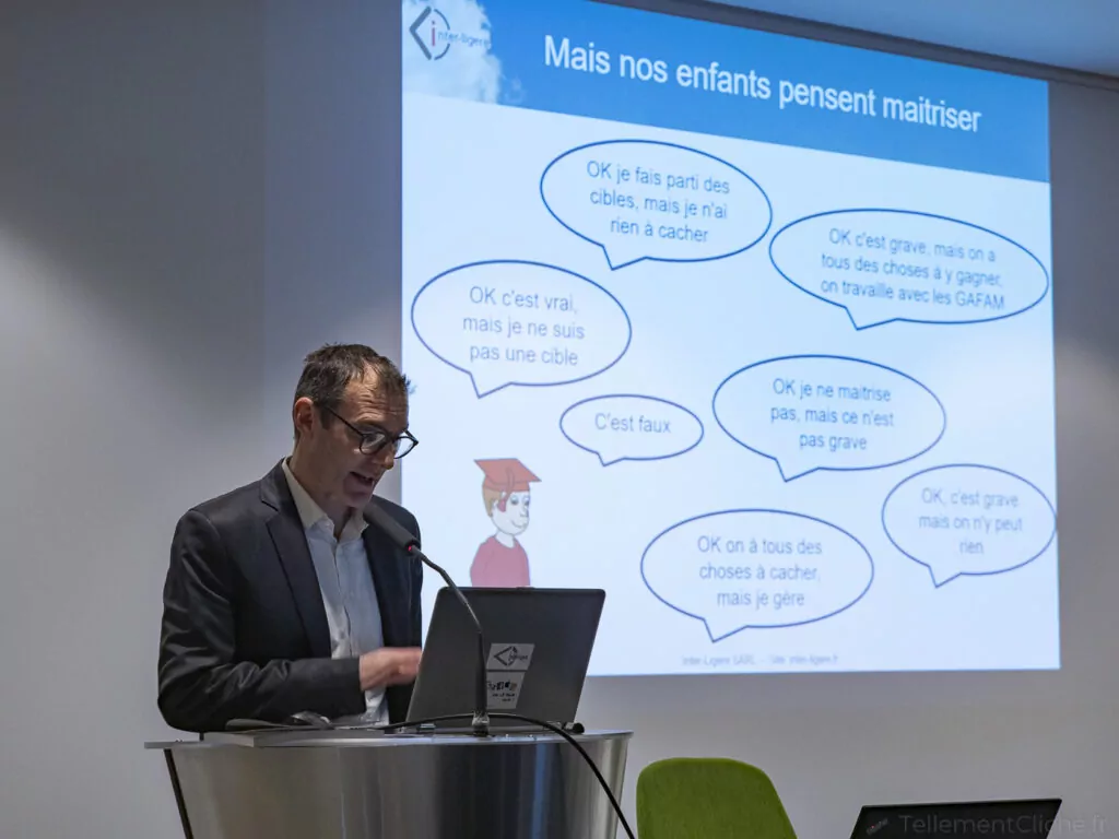 Un homme en costume parle sur un podium avec un microphone. Derrière lui, une diapositive française sur l'éducation numérique montre des bulles de texte sur la perception des risques numériques par les enfants et un enfant de bande dessinée portant un bonnet de fin d'études. - Rotary Club Paris Agora