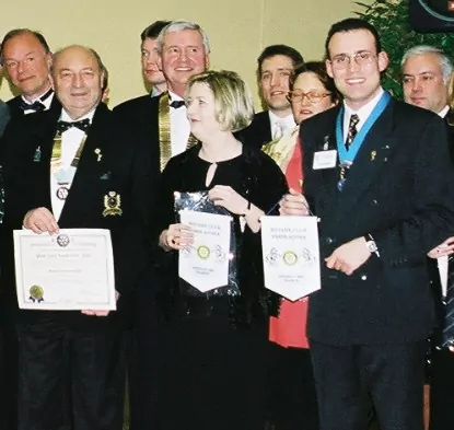 Un groupe de personnes en tenue de soirée se tient ensemble à l'intérieur, certaines tenant des certificats et des bannières du Rotary Club, posant pour une photo lors d'une cérémonie de remise de prix ou de reconnaissance célébrant l'engagement de la collectivité. - Rotary Club Paris Agora